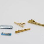 Fem slipsnål i forskellige designs på hvid baggrund.