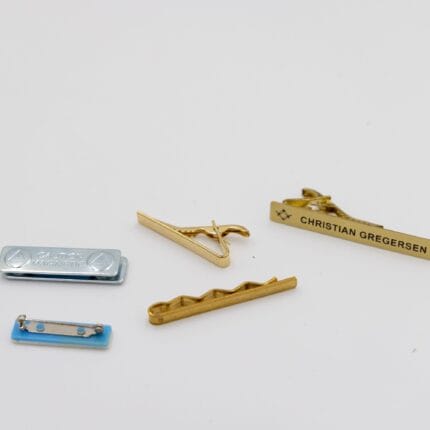 Fem slipsnål i forskellige designs på hvid baggrund.