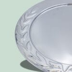 Sølvtallerken med dekorativ kant på grøn baggrund.