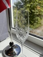 Indgraveret champagneglas ved vindue med flag.